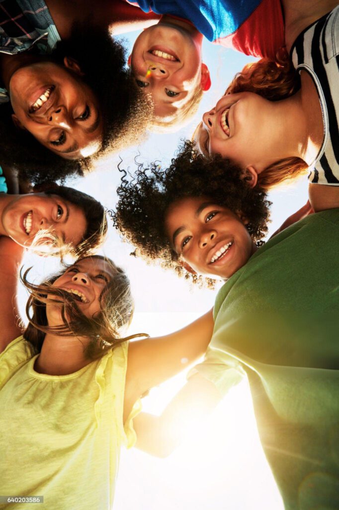 A group of kids in a circle looking down at the camera.